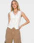 Woman wearing a white sleeveless top and beige pants on a plain background