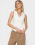 Woman wearing a white sleeveless blouse and beige pants on a light gray background