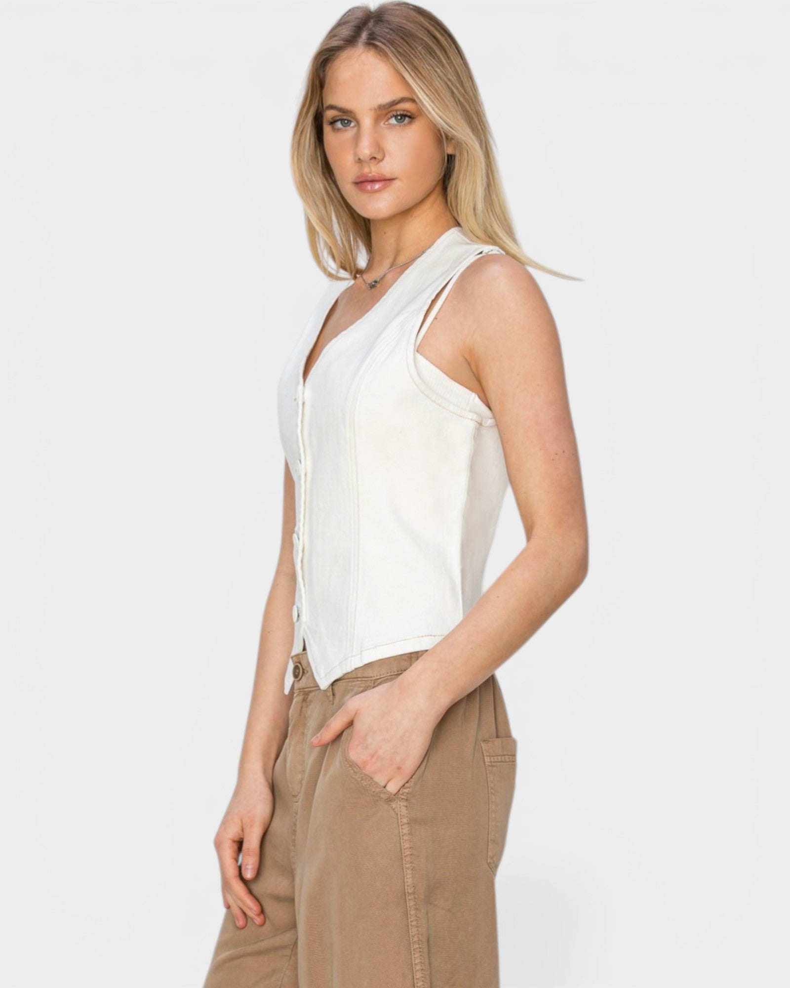 Woman wearing a white sleeveless top and beige pants on a plain background
