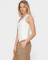 Woman wearing a white sleeveless top and beige pants on a plain background