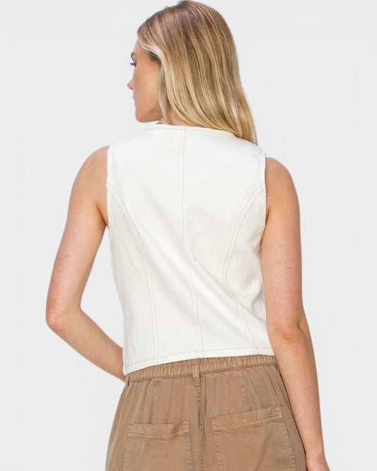 Person wearing a white sleeveless top and beige pants on a plain background