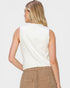 Person wearing a white sleeveless top and beige pants on a plain background