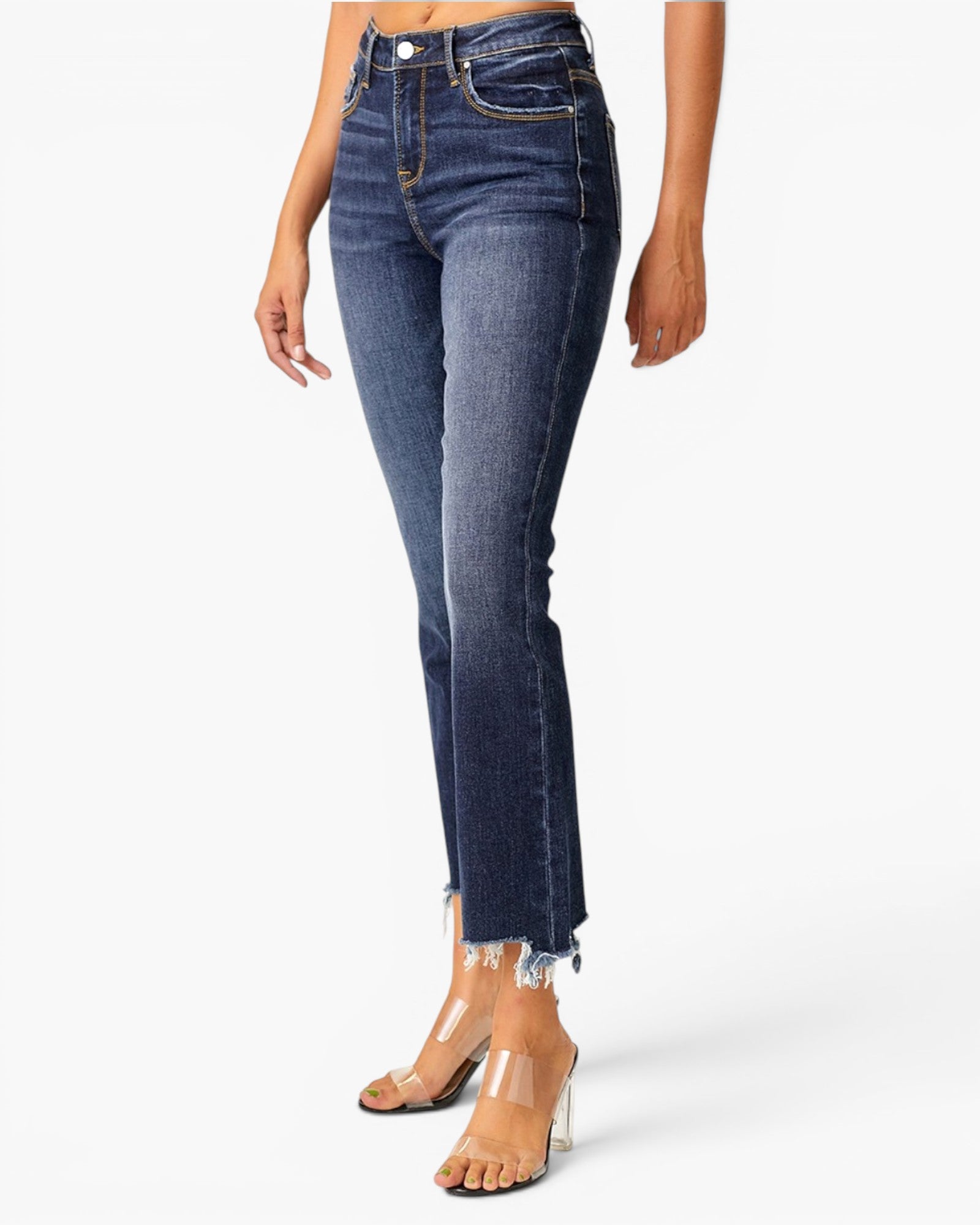 A model wearing dark blue high-waisted cropped flare jeans with a raw frayed hem, paired with clear high-heeled sandals, against a plain white studio background.