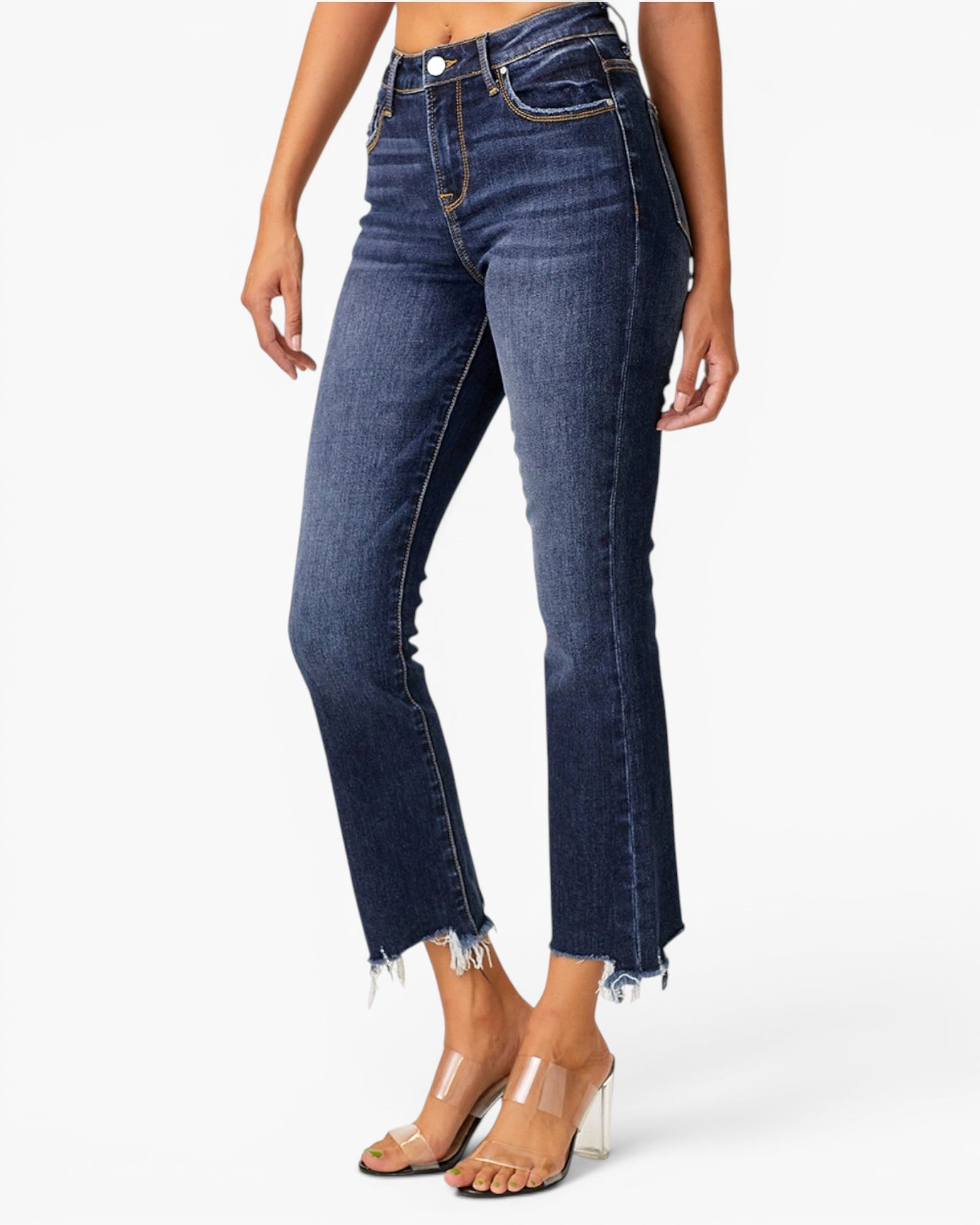 A model wearing dark blue high-waisted cropped jeans with a raw frayed hem, paired with clear high-heel sandals, against a plain white studio background.
