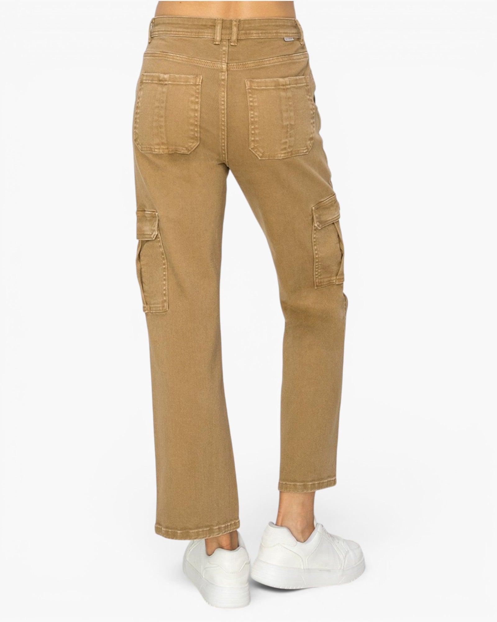 A person shown from the waist down wearing tan cargo-style jeans with flap side pockets and white sneakers, photographed against a plain light gray studio background.