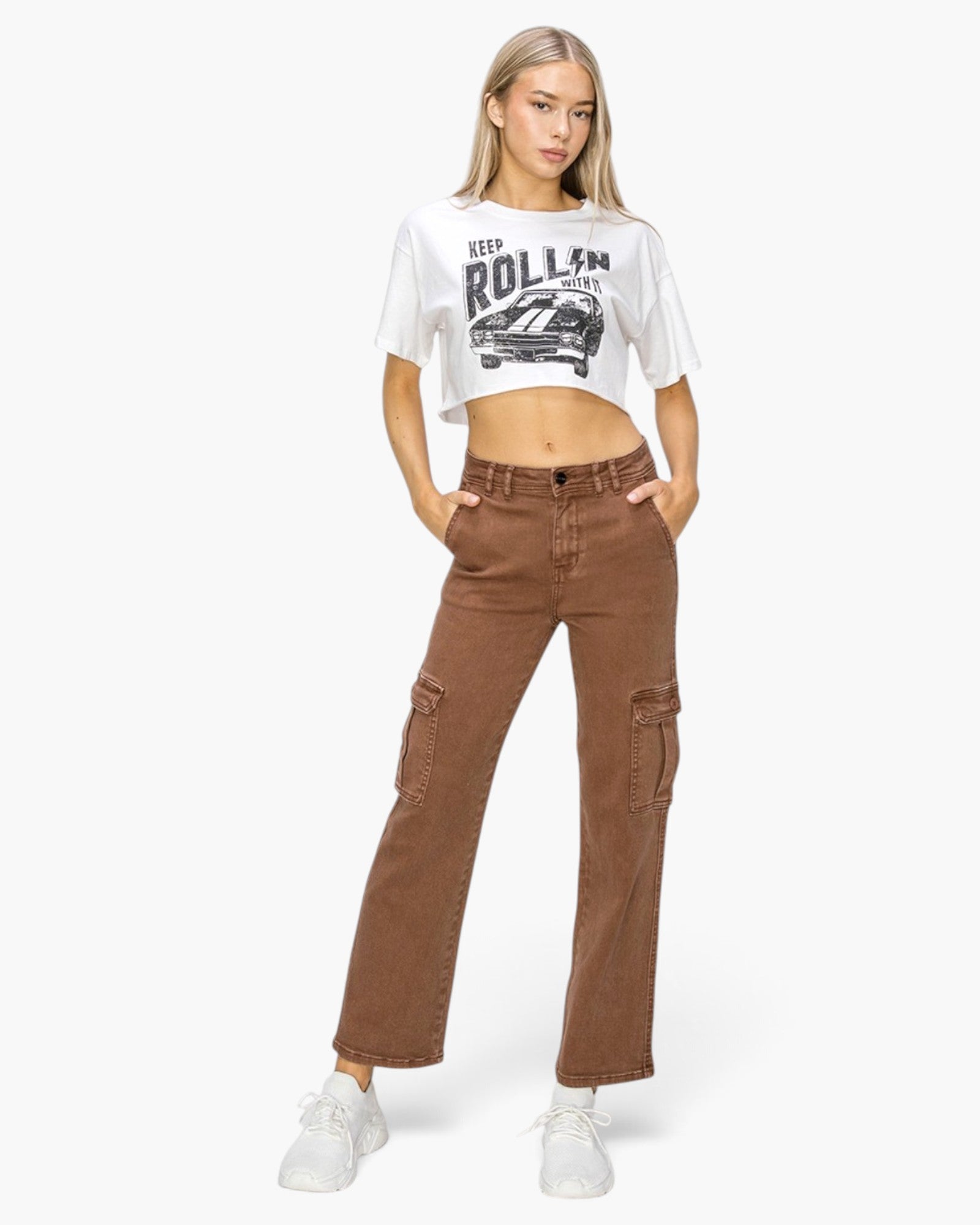 A model wearing a white cropped graphic t-shirt and brown wide-leg cargo pants, standing against a light gray studio background.