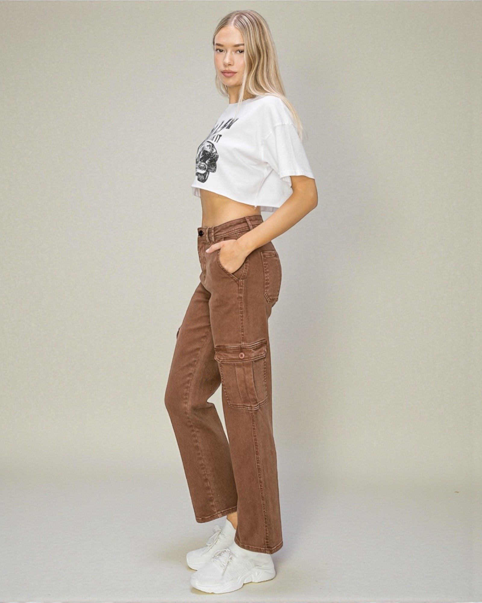 Woman wearing a white cropped top and brown pants on a plain background