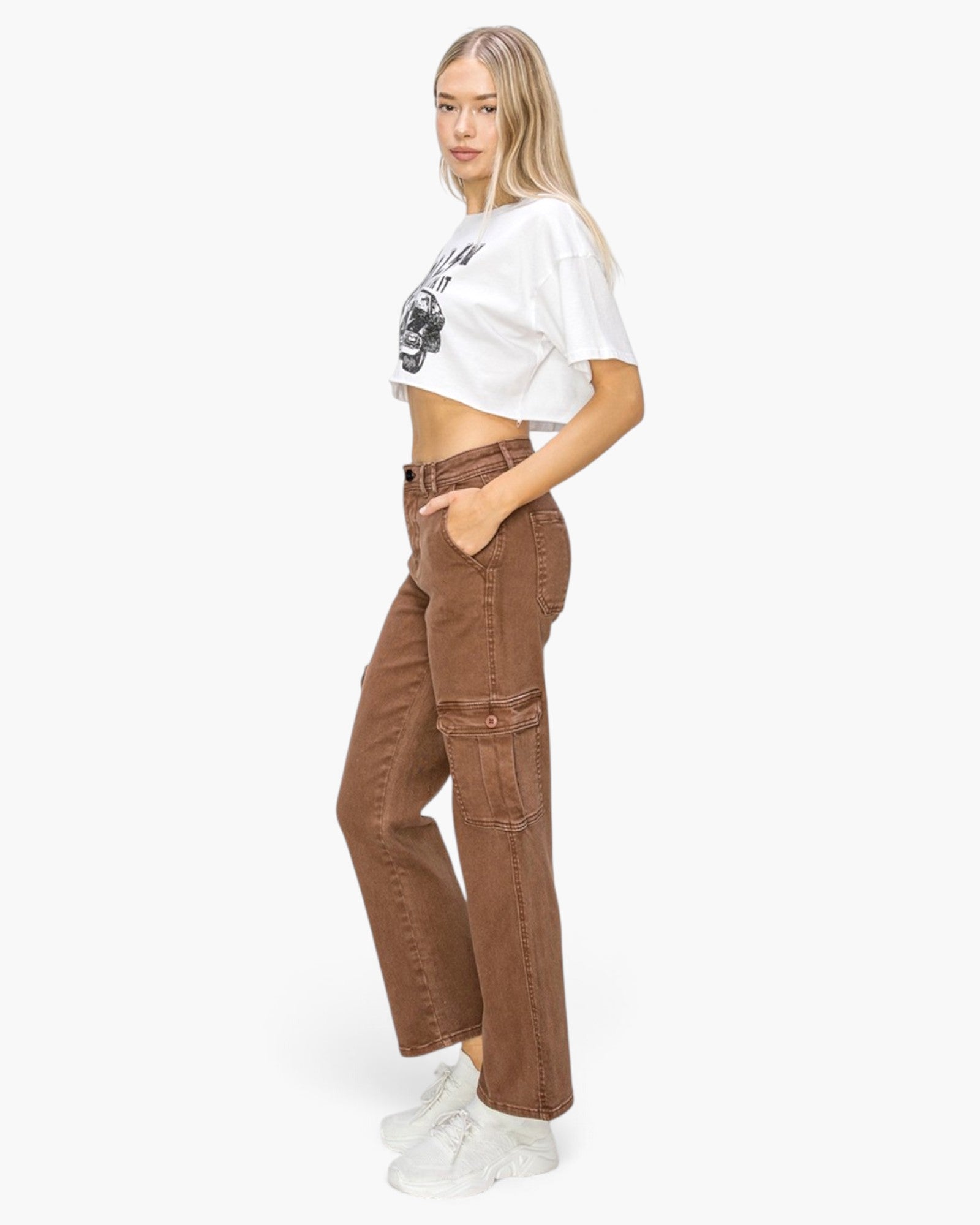 A woman modeling a white cropped graphic t-shirt and brown high-waisted cargo pants against a plain white studio background.