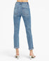 Rear view of a person wearing light blue denim jeans with rolled cuffs and white heeled sandals against a plain white studio background.