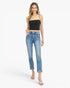 A woman modeling a pair of light-wash blue cropped jeans with rolled cuffs, paired with a black spaghetti-strap crop top and white sandals, against a plain white studio background.