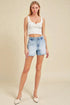 Woman wearing a white lace top and denim shorts on a beige background