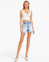 A woman modeling a white textured crop top and light-wash denim shorts against a plain white studio background.