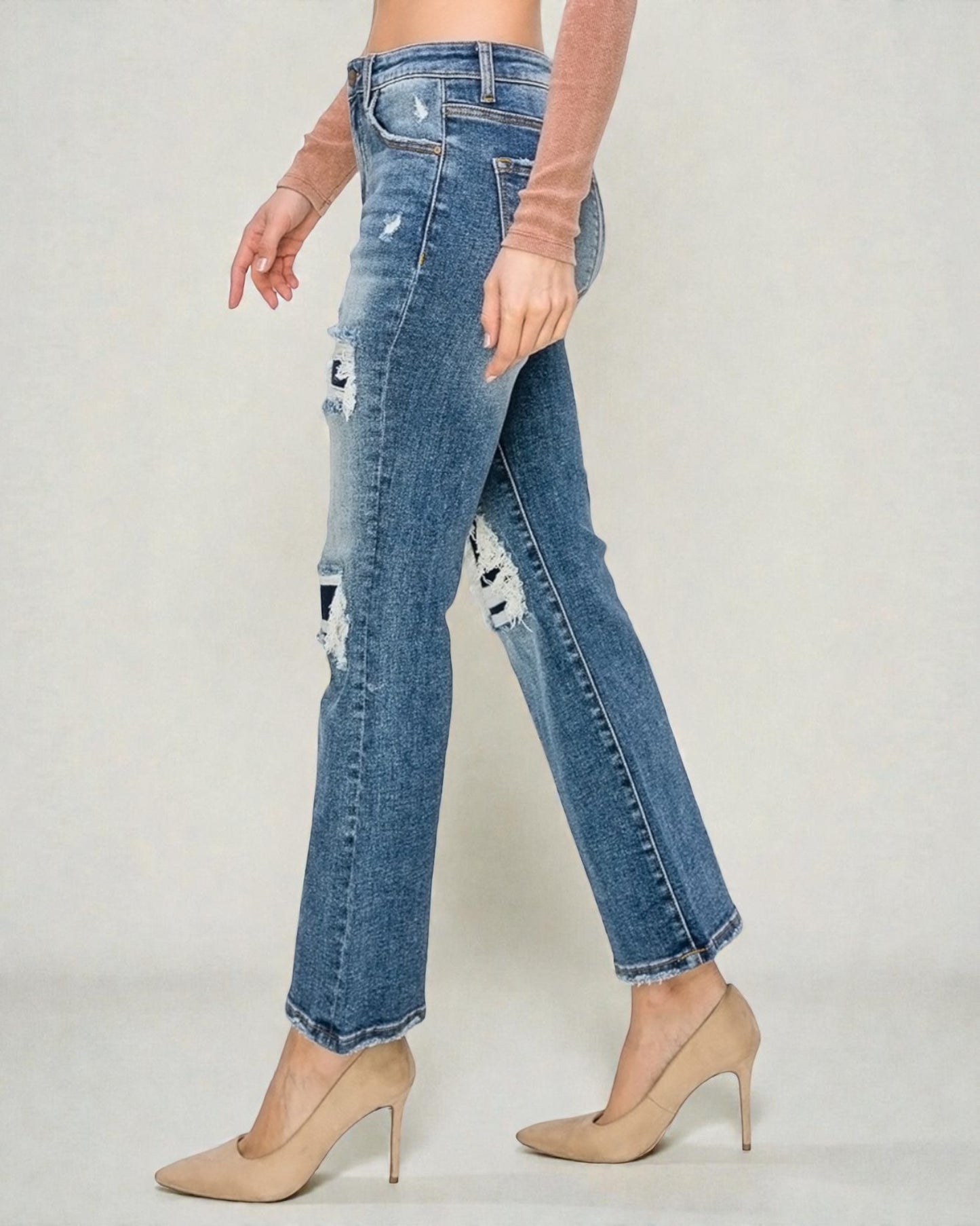 Distressed blue jeans worn by a person on a plain background