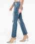 A model wearing a pair of high-waisted, distressed blue denim jeans with frayed hems and ripped details on the thighs and knees, styled with beige high heels and a sheer beige long-sleeve top against a plain white background.