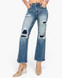 A model wearing a pair of medium-wash blue denim jeans with distressed rips on the thighs and knees, paired with beige high heels against a plain white background.
