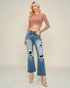 Woman wearing a pink long-sleeve top and distressed blue jeans on a beige background