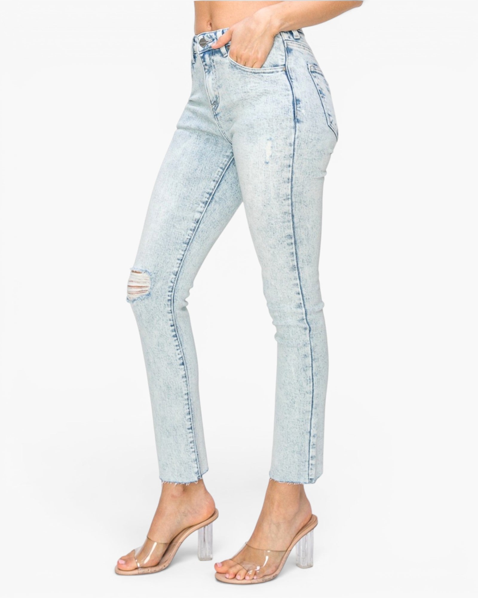 Light-wash distressed skinny jeans with a faded blue wash, modeled on a person wearing clear high-heel sandals against a plain white background.