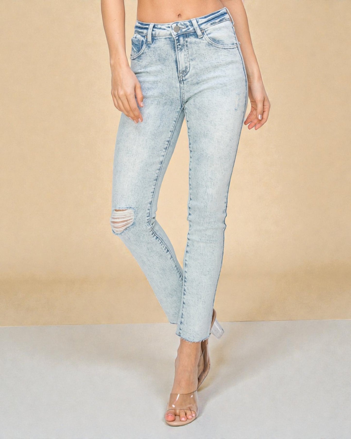 Light blue distressed jeans worn by a person on a beige background