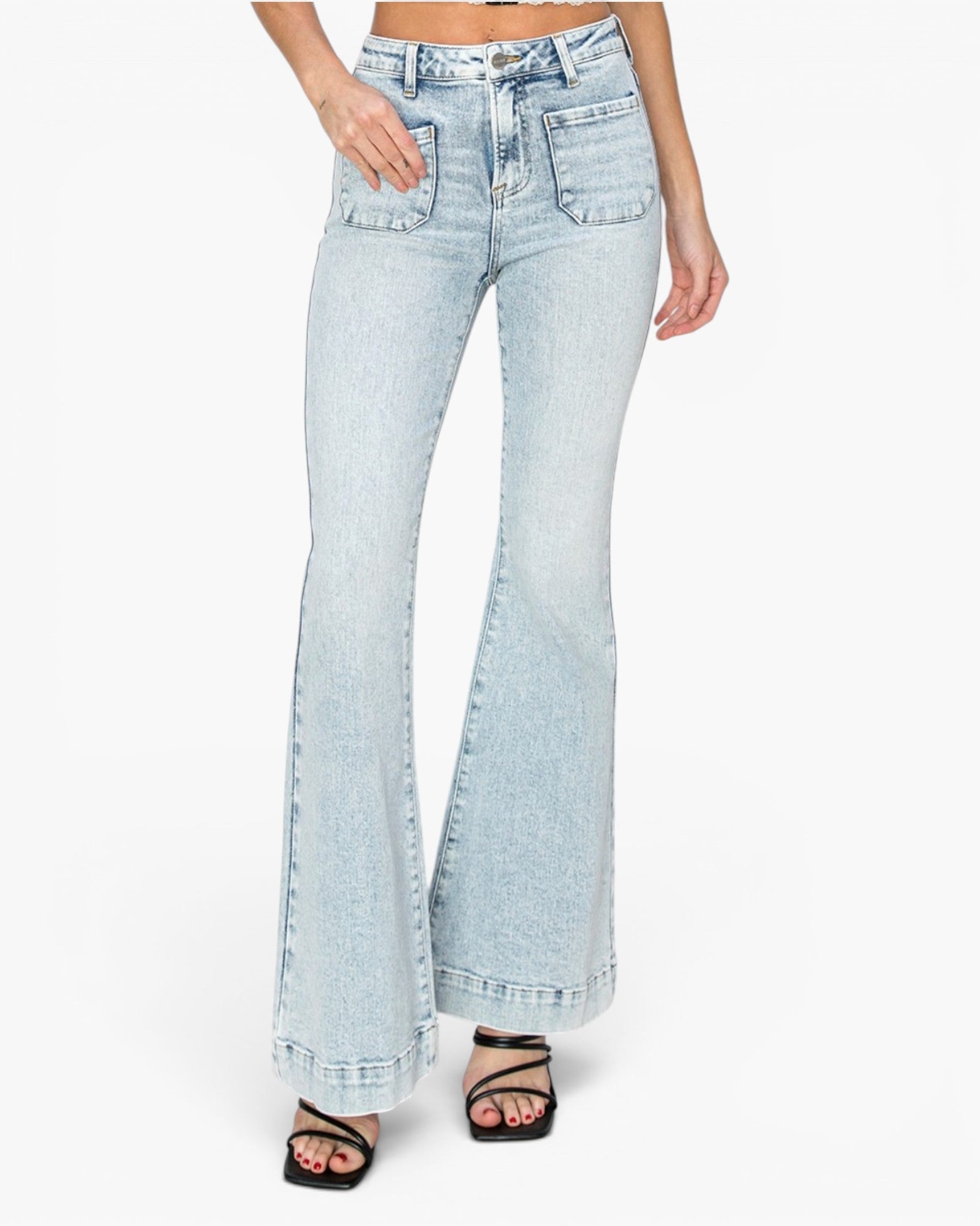 A model wearing light-wash blue flare jeans with rolled cuffs and black strappy sandals, shown from the waist down on a plain white studio background.