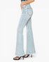 A side profile view of a model wearing light-wash blue high-rise flare jeans with rolled hems and black strappy high-heeled sandals, set against a plain white background.