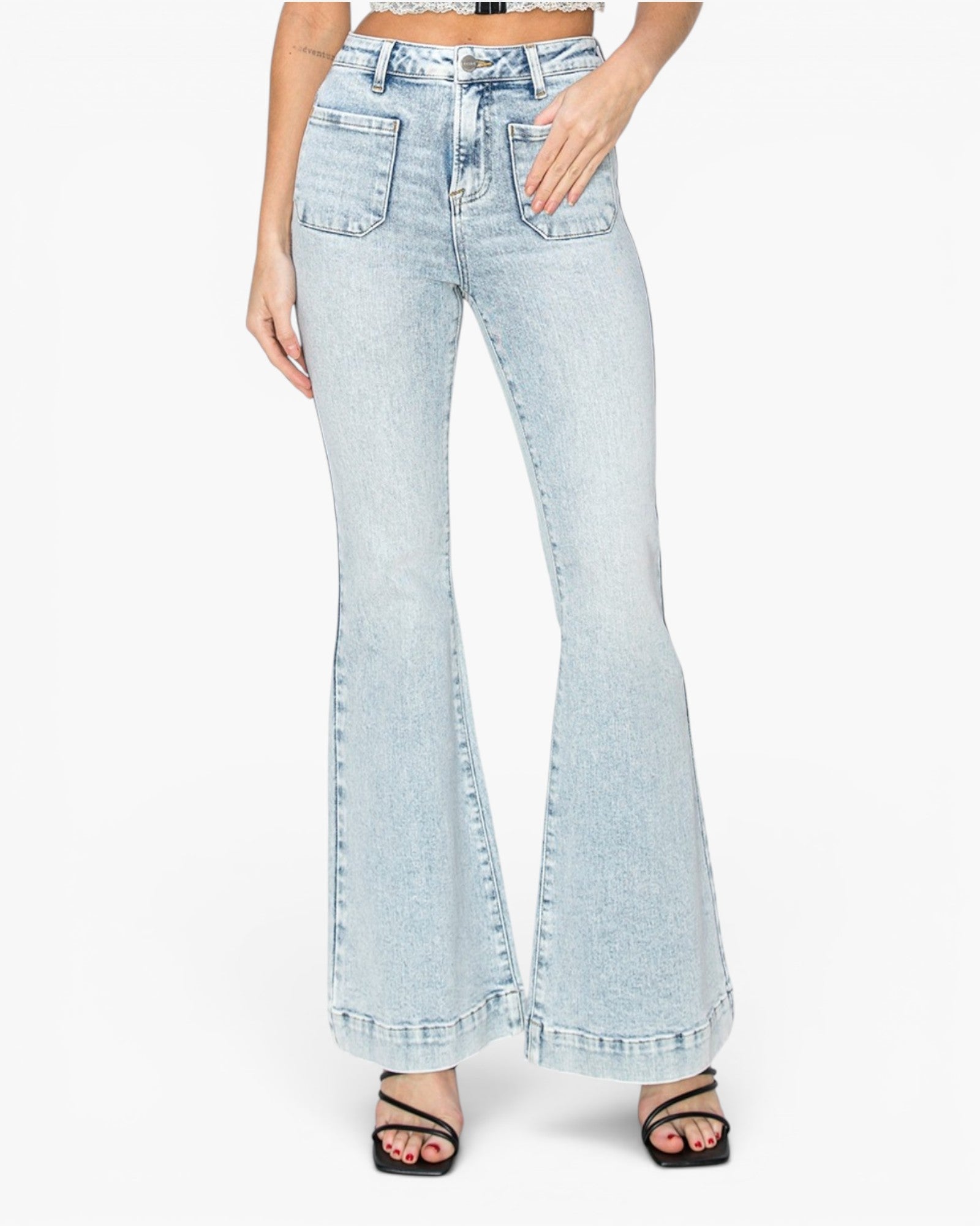A model wearing light-wash blue denim flare jeans with a high waist and wide flared legs, paired with black strappy heels against a plain white background.