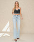 Woman wearing a black beaded top and light blue jeans on a beige background