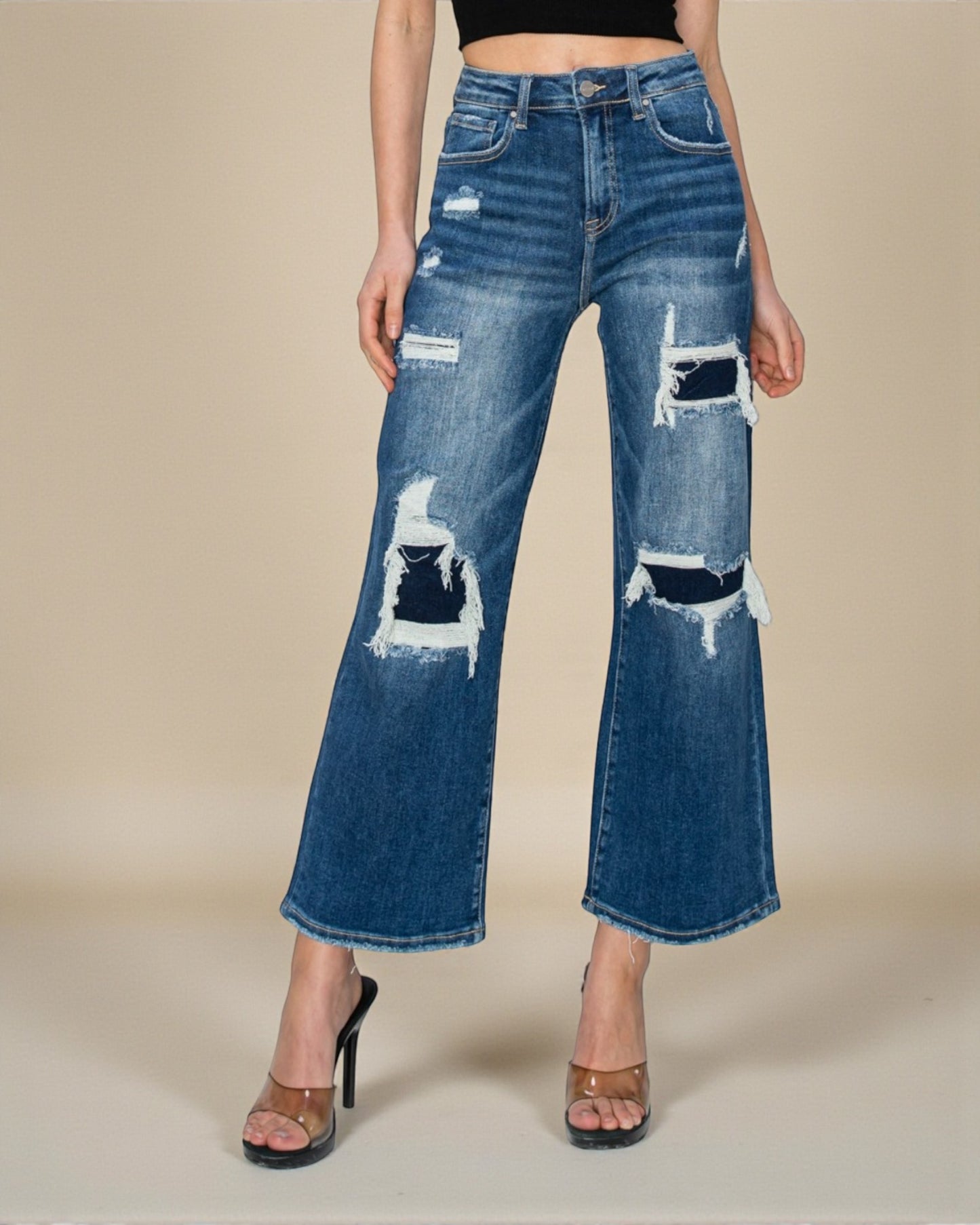 Distressed blue jeans worn by a person on a beige background