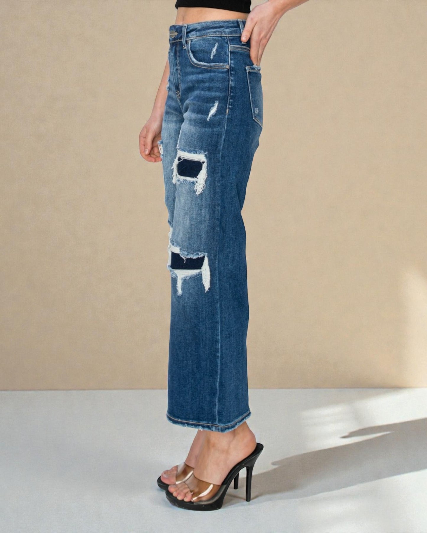 Blue distressed jeans worn by a person on a beige background