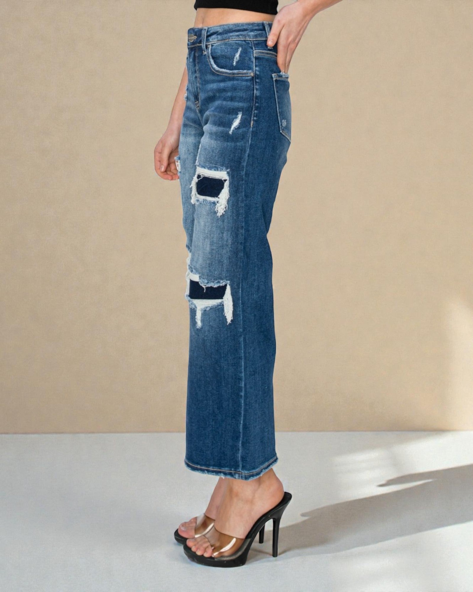 Blue distressed jeans worn by a person on a beige background