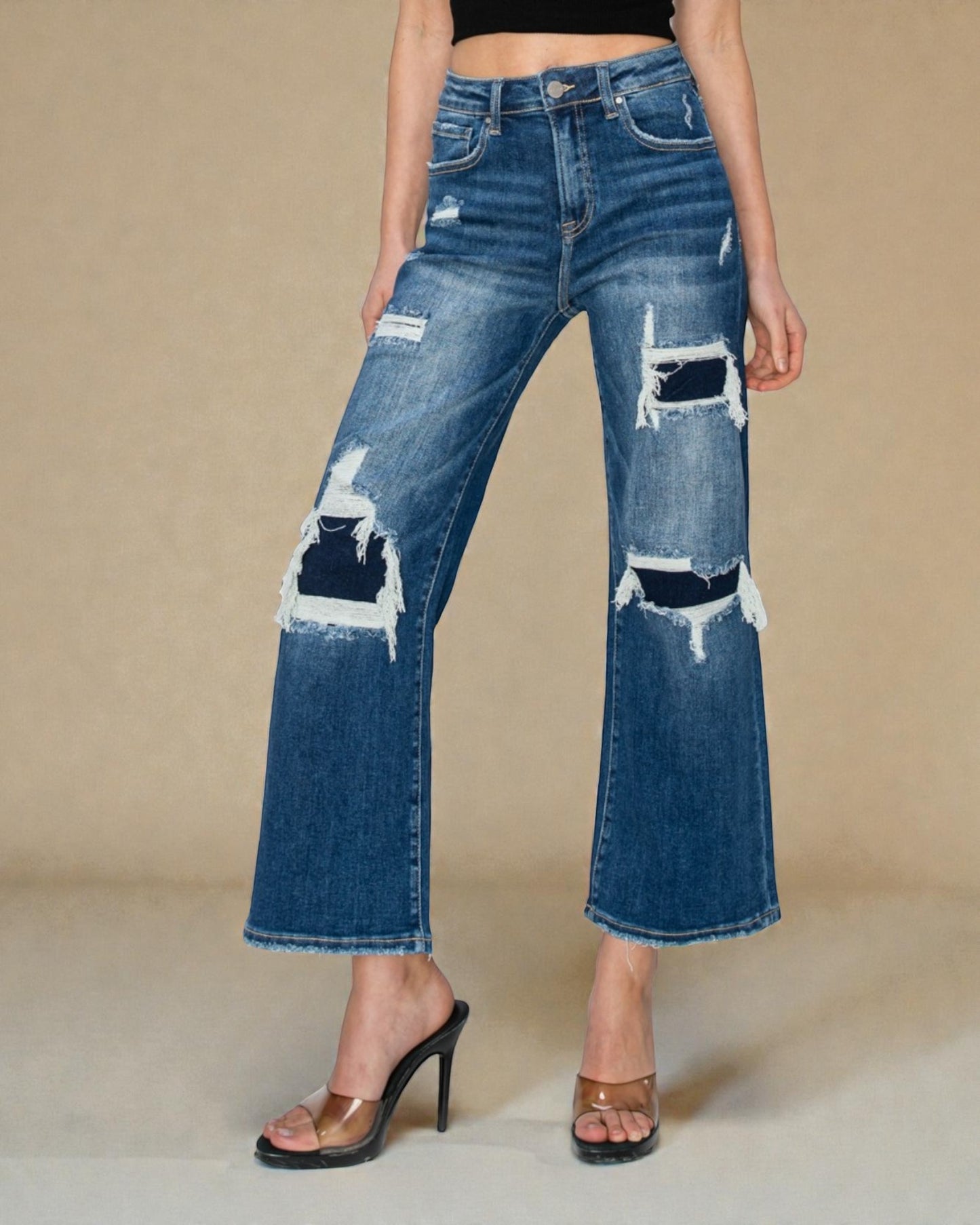 Person wearing distressed blue jeans on a beige background