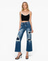 A model wearing a pair of high-waisted, wide-leg blue jeans with distressed rips and frayed details, styled with a black camisole top and brown heeled sandals against a light gray background.