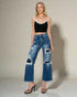 Woman wearing a black crop top and distressed blue jeans against a neutral background