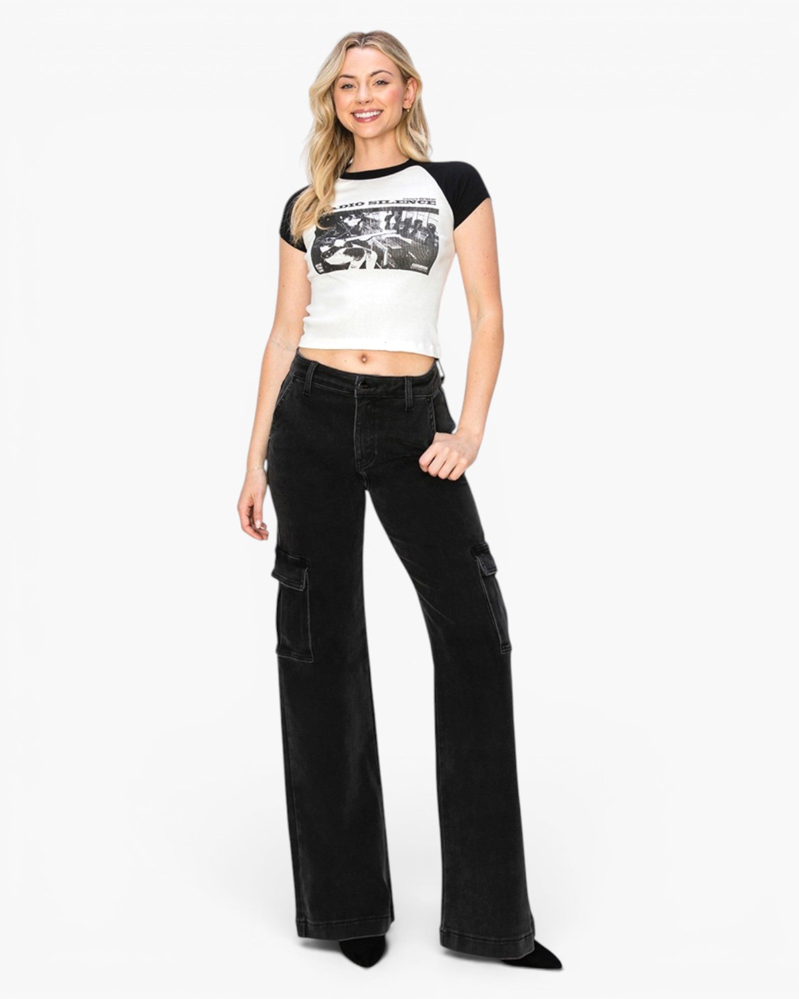 A woman modeling a white and black raglan crop top with a black graphic print and black wide-leg cargo pants against a plain white studio background.