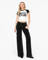 A woman modeling a white and black raglan crop top with a black graphic print and black wide-leg cargo pants against a plain white studio background.