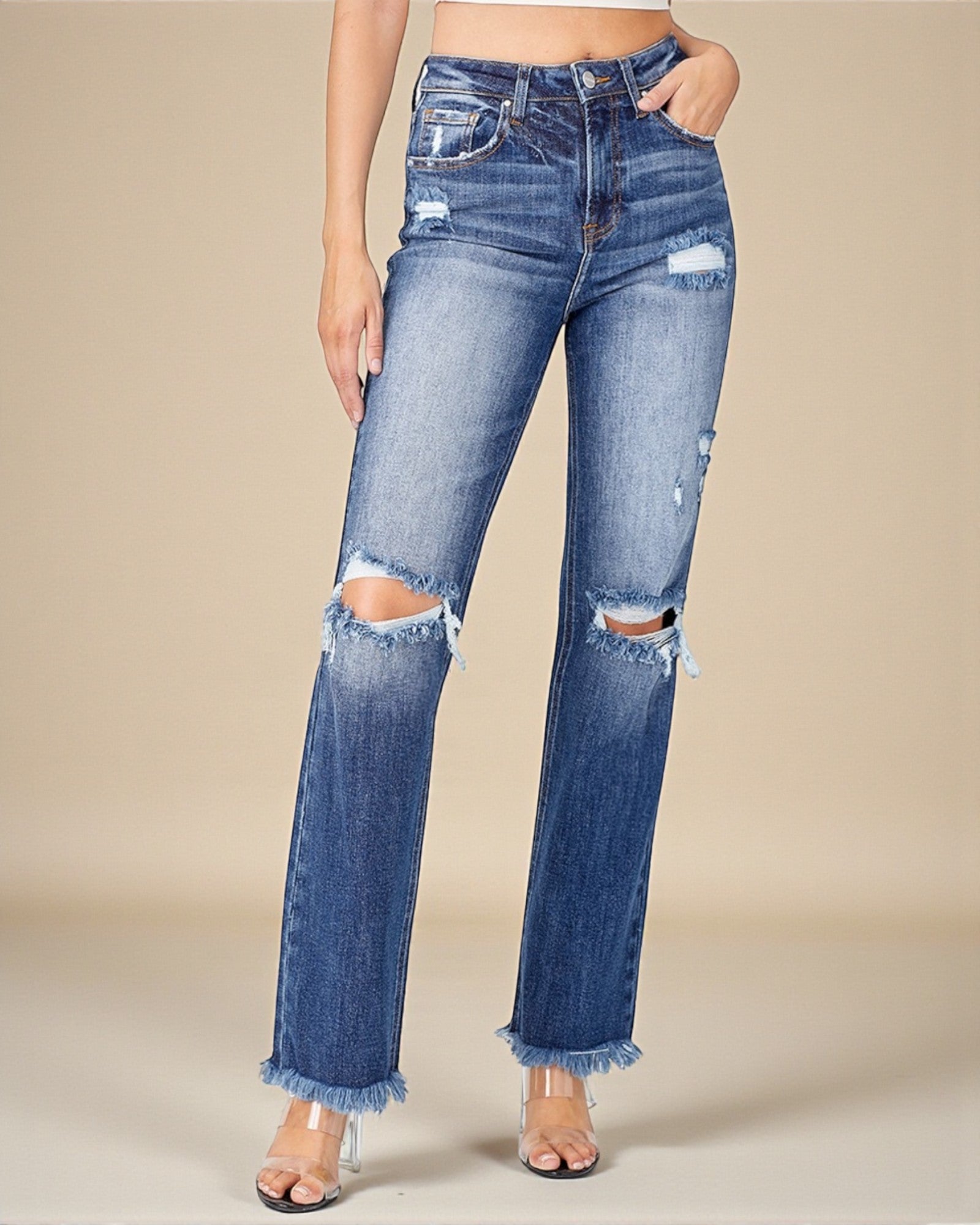Ripped blue jeans worn by a person on a beige background