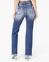 Rear view of a model wearing high-waisted, straight-leg blue denim jeans with distressed details and frayed hems, paired with clear high-heeled sandals against a white studio background.
