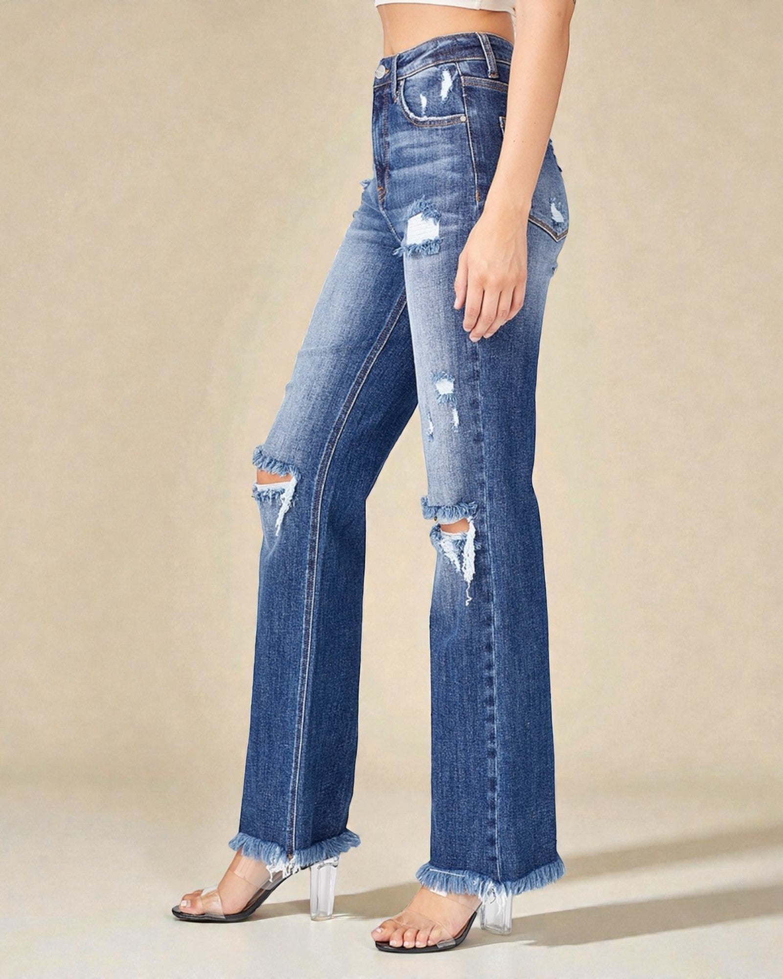 Blue distressed jeans worn by a person on a beige background