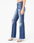 A model wearing high-waisted, distressed blue flare jeans with frayed hems and ripped knees, paired with clear-strap high heels against a plain white background.