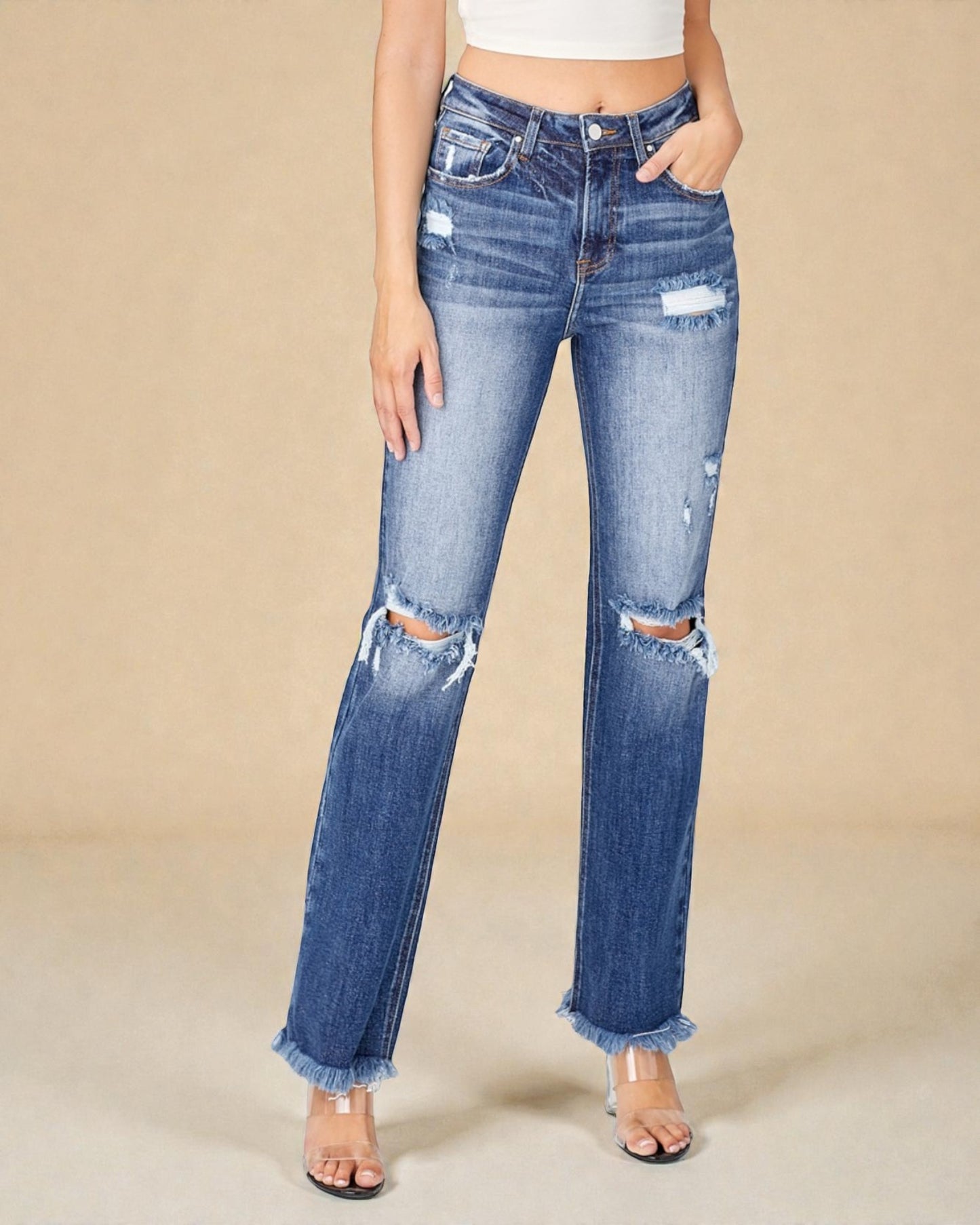 Person wearing distressed blue jeans on a beige background