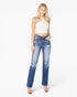A woman modeling a pair of high-waisted, distressed blue jeans with a straight-to-flare leg, paired with a white halter crop top and clear high-heeled sandals, against a plain white studio background.