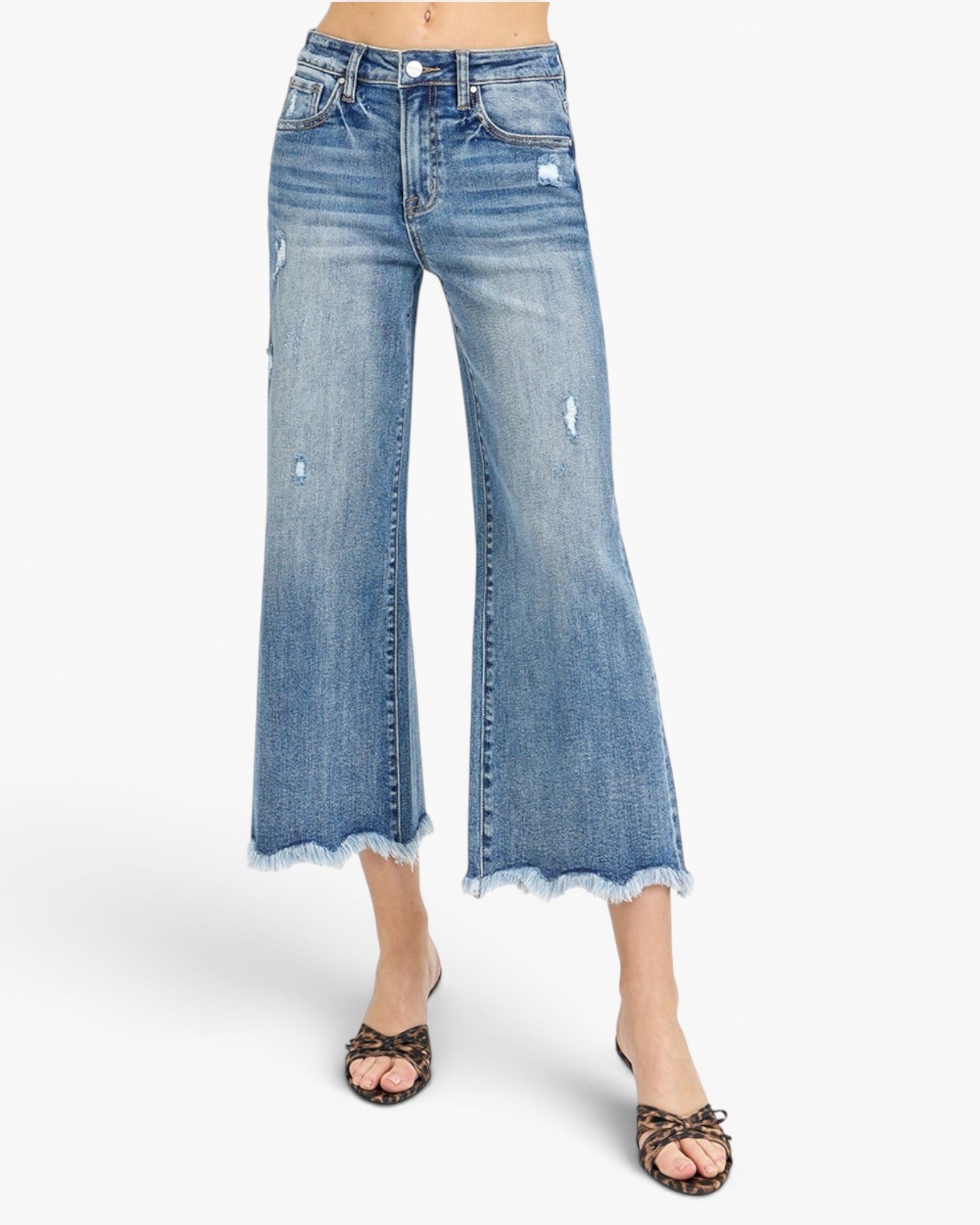 A model wearing light blue cropped flare jeans with a frayed hem and distressed details, paired with leopard-print flat sandals, against a plain white background.