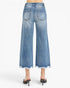 Back view of a model wearing light blue wide-leg cropped denim jeans with a frayed hem and distressed details on the back pockets, paired with black pointed-toe mule heels.
