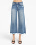 A model is wearing a pair of wide-leg, cropped blue denim jeans with distressed details and a frayed hem, paired with leopard-print heeled sandals against a plain white background.