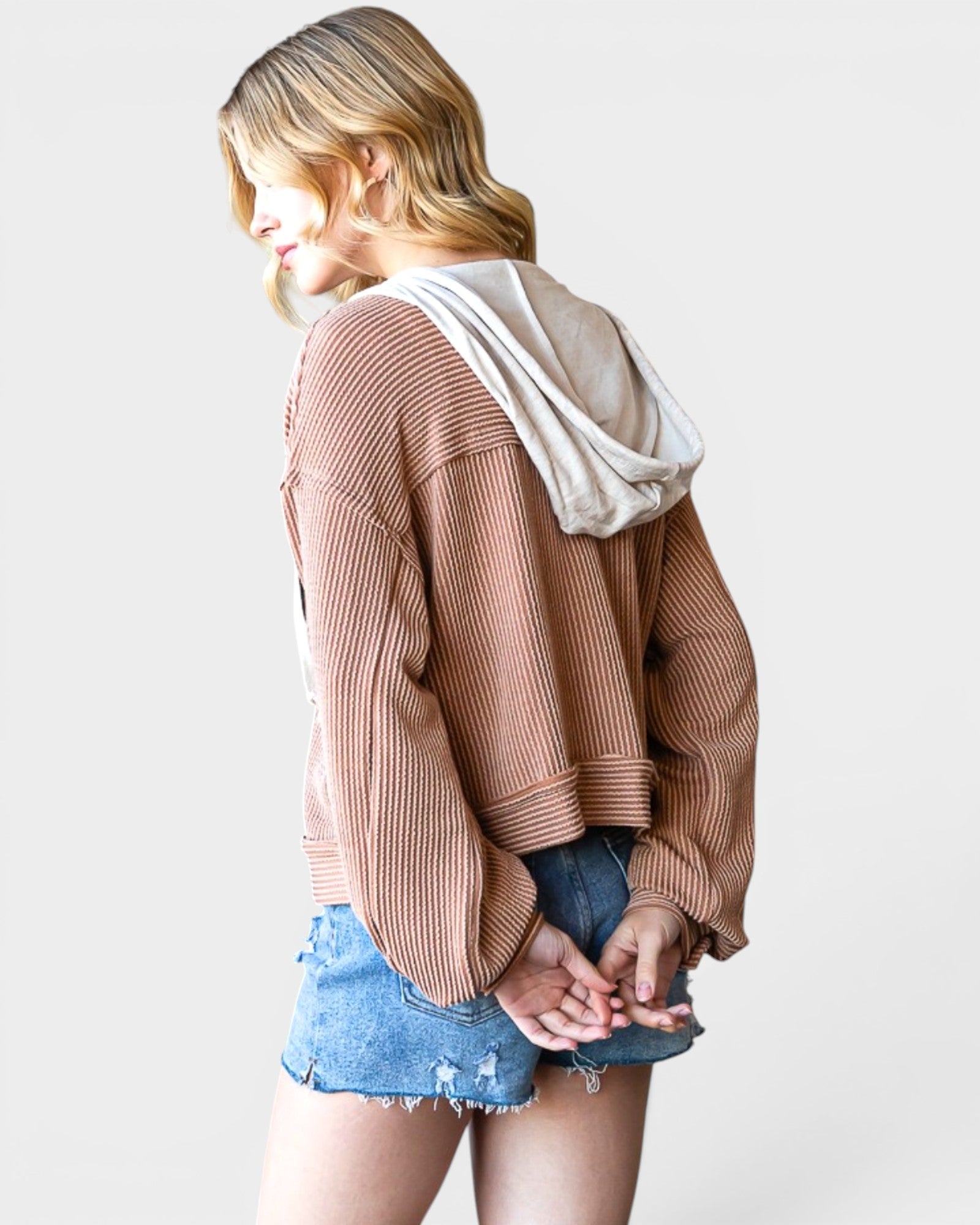 Woman wearing a brown ribbed sweater and denim shorts on a white background