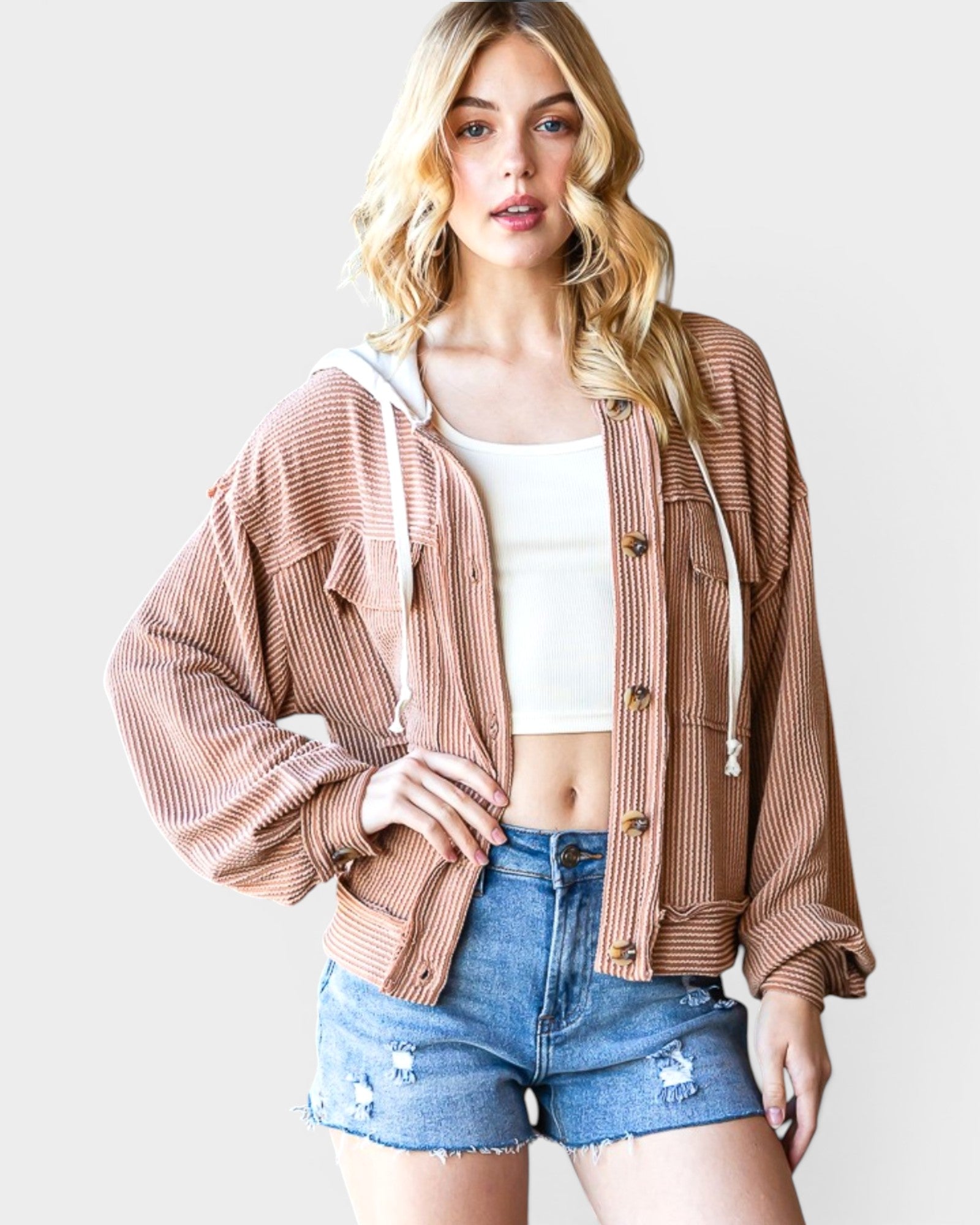 Woman wearing a brown corduroy jacket over a white crop top and denim shorts on a plain background