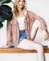 Woman sitting on a bench wearing a pink jacket, white top, and denim shorts.