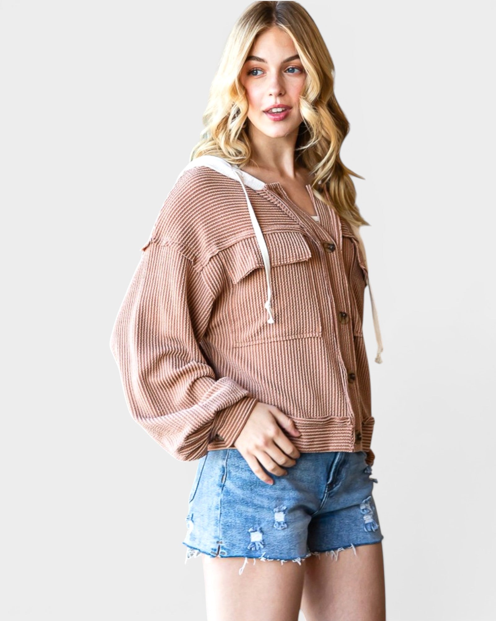 Woman wearing a brown ribbed knit cardigan and denim shorts on a white background