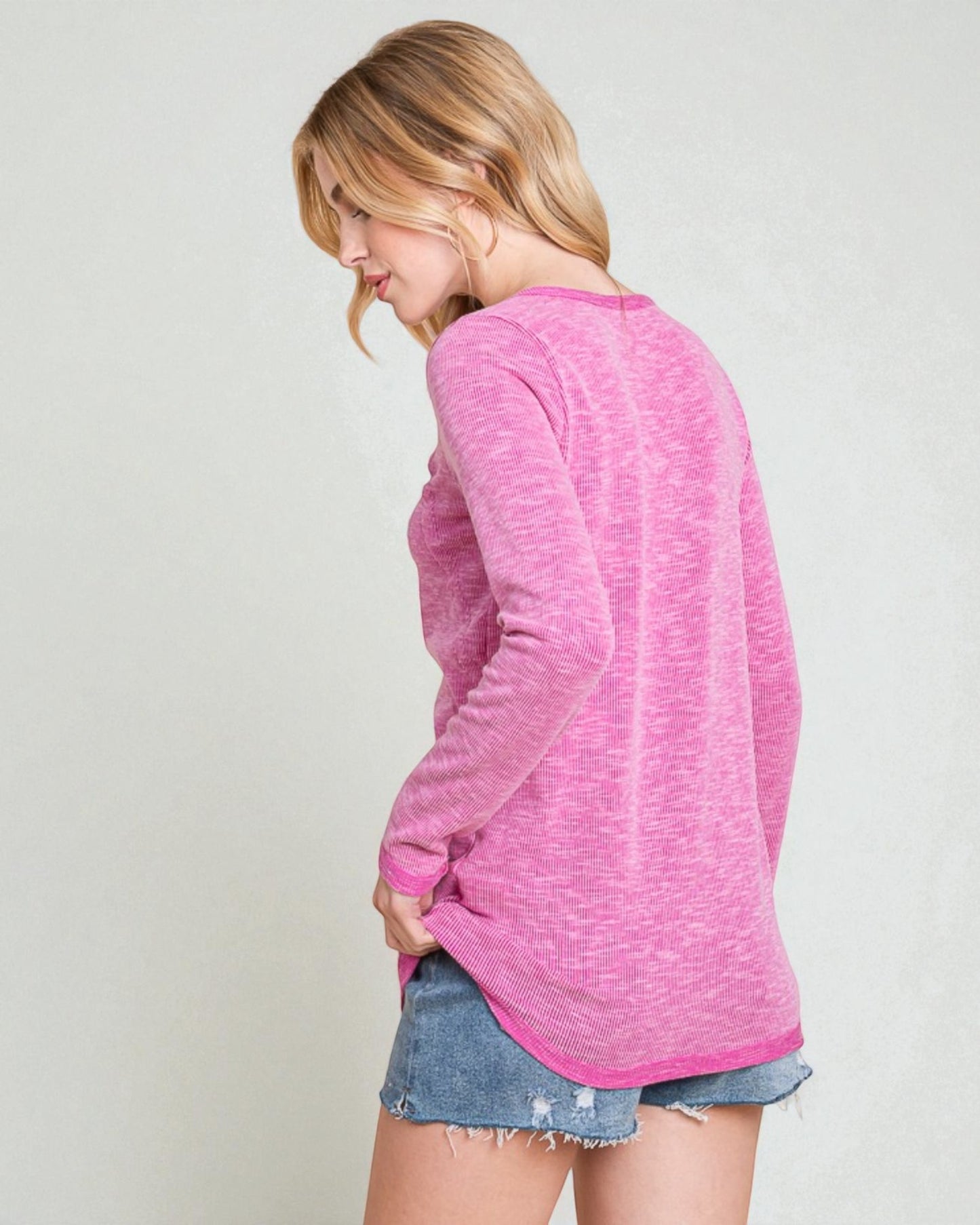 Woman wearing a pink long-sleeve top and denim shorts on a plain background