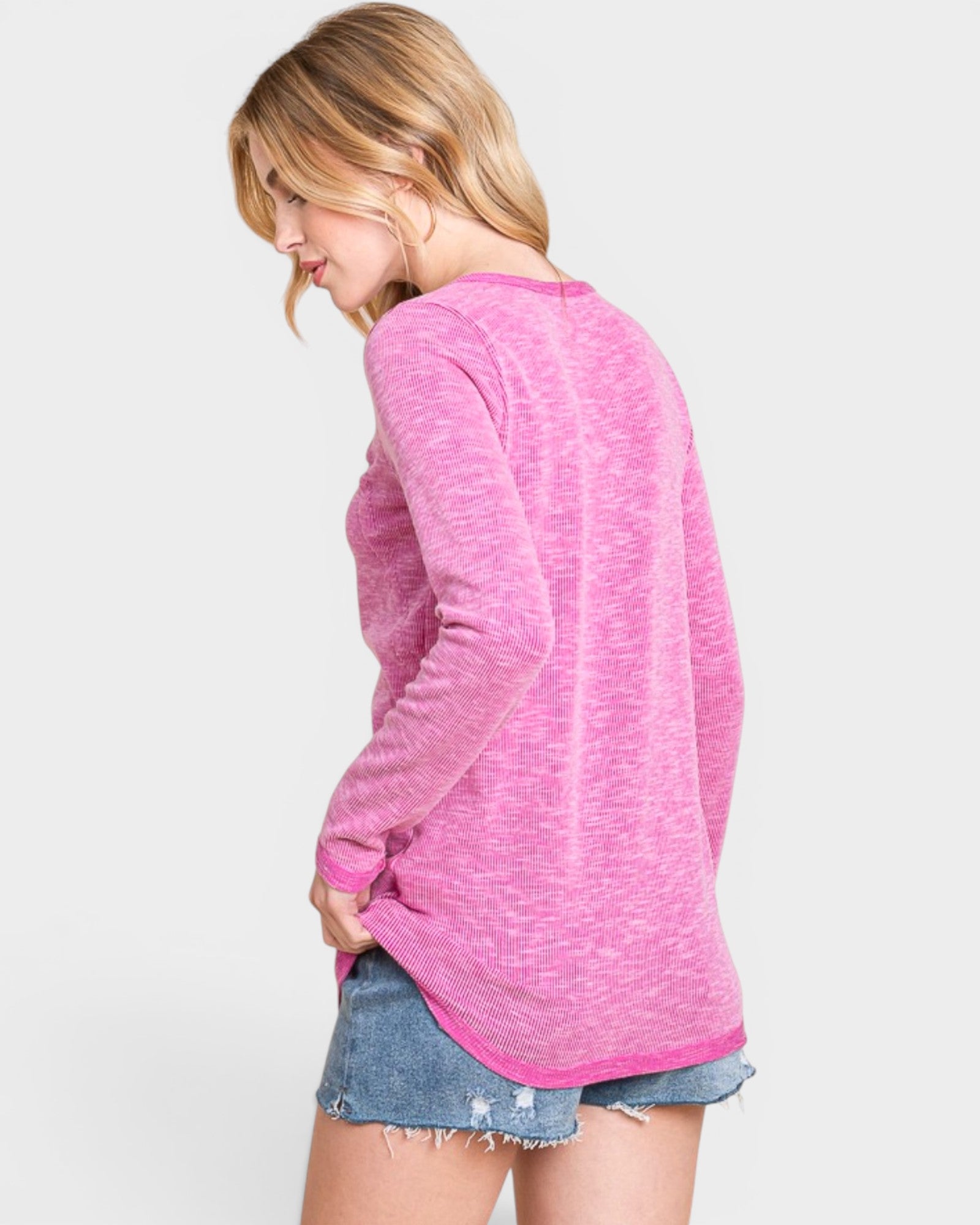 Woman wearing a pink sweater and denim shorts on a light gray background