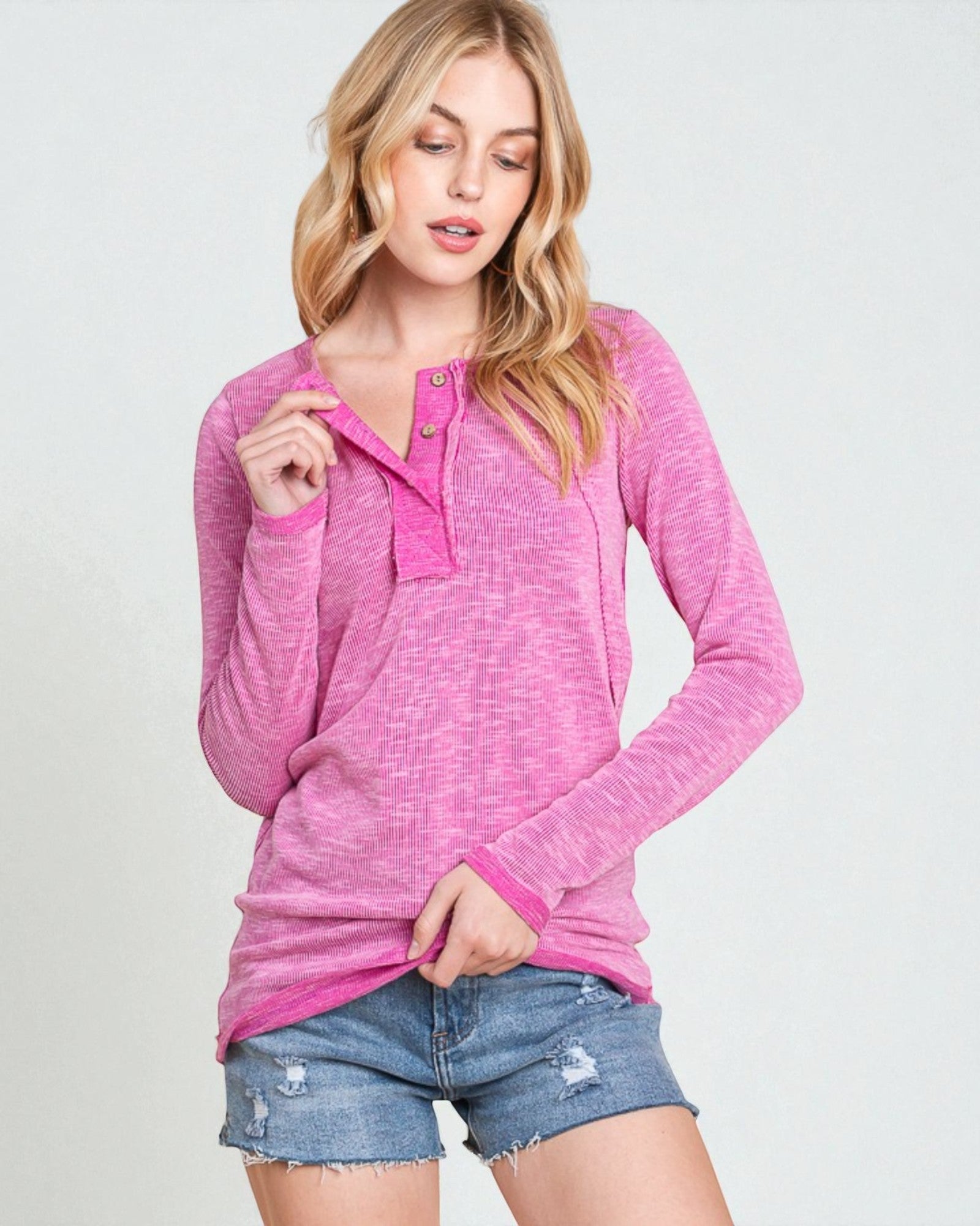 Woman wearing a pink long-sleeve top and denim shorts on a light gray background